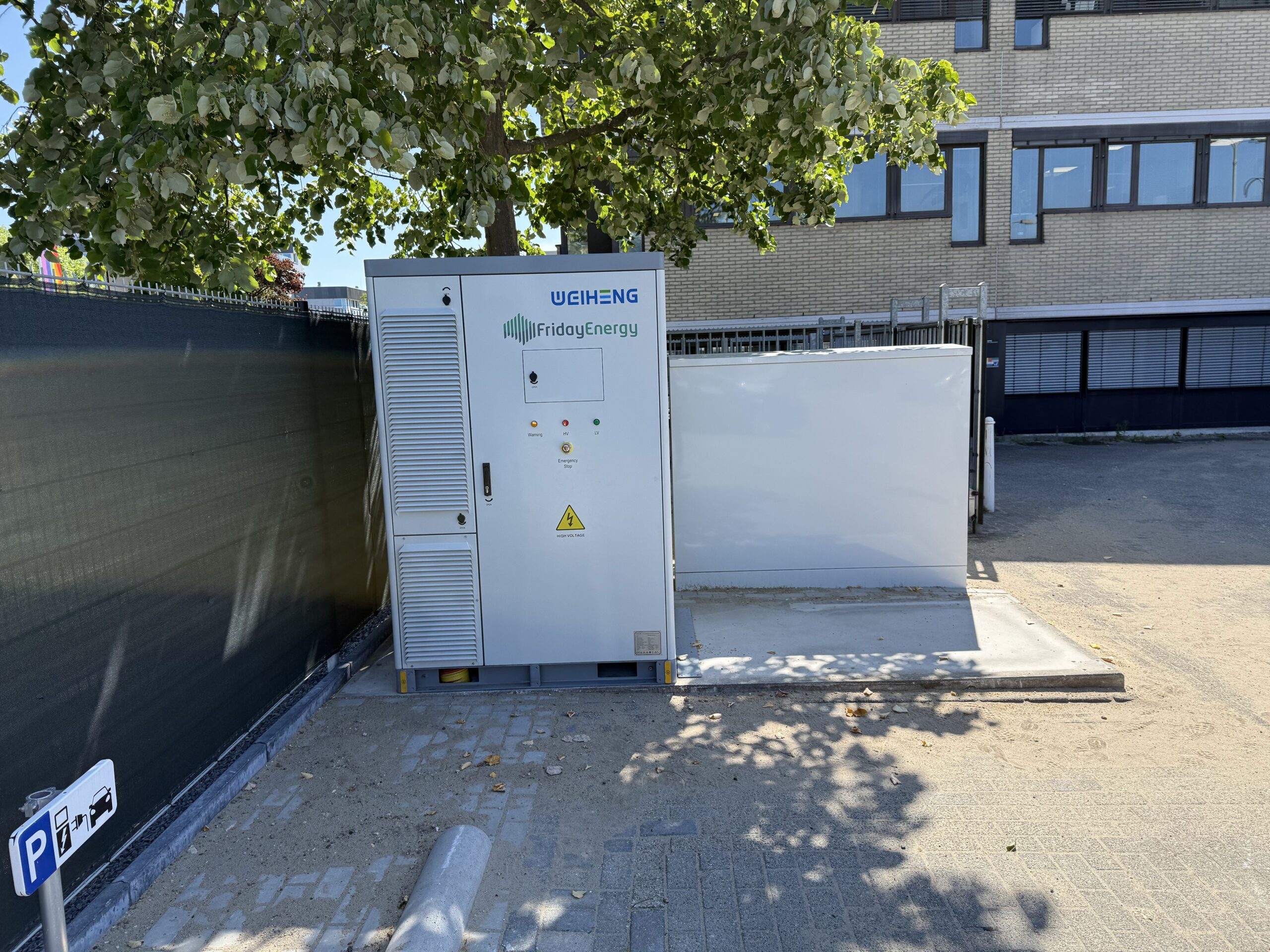 Batterijsysteem van Friday Energy geplaatst bij een bedrijfspand, met laadpunt op de parkeerplaats