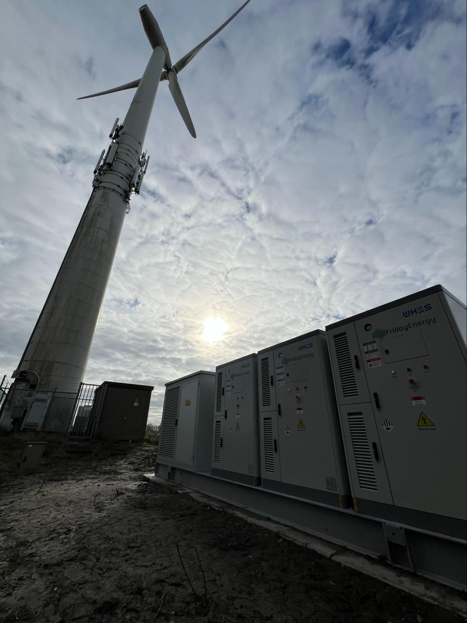 Batterijen van Friday Energy naast de windturbine bij Nagele, tegenlicht met bewolkte lucht