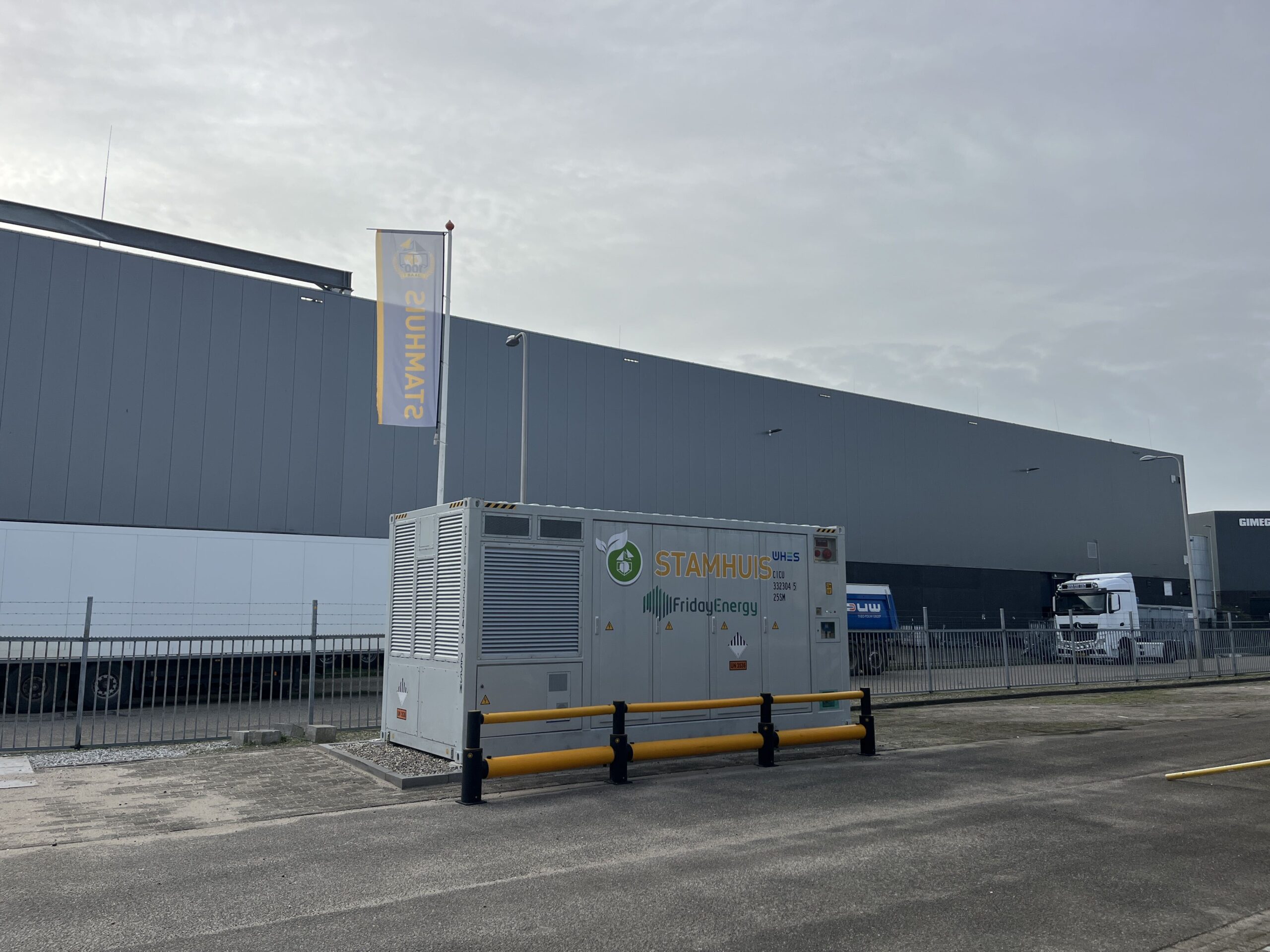 Batterijopslag bij Stamhuis in Utrecht · batterijcontainer met de logo's van Stamhuis en Friday Energy naast de bedrijfshal